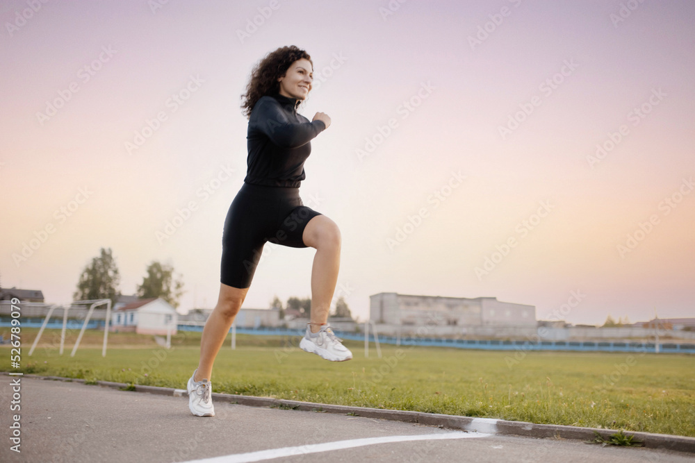 curly woman runner, runs around the stadium in sportswear. Morning running.