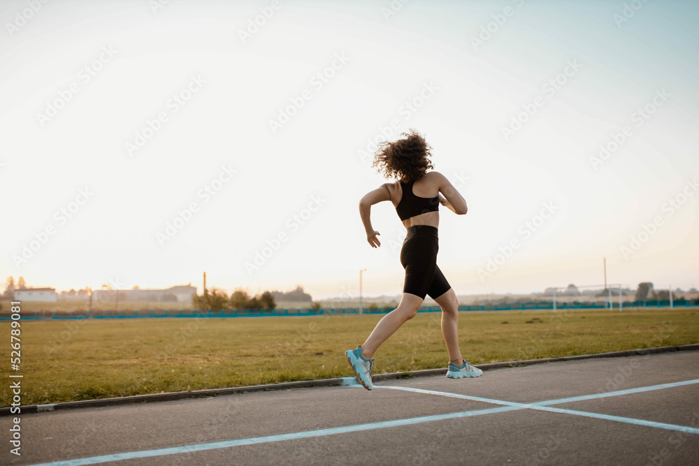 young sports woman runs in the stadium in sportswear, sportswoman training.