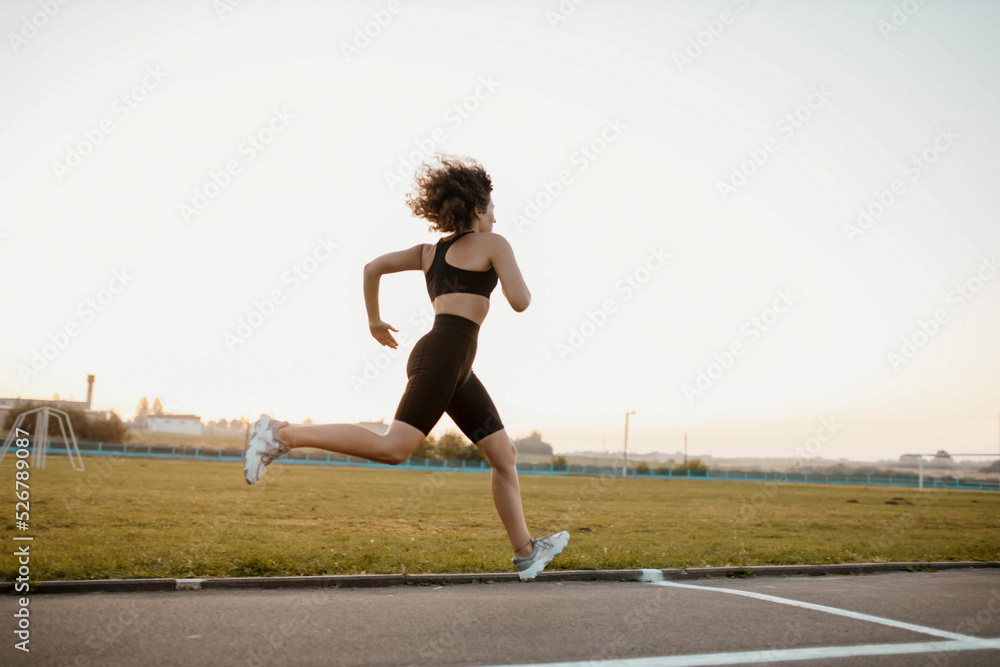 young sports woman runs in the stadium in sportswear, sportswoman training.