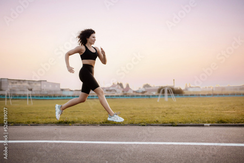 curly woman runner, runs around the stadium in sportswear. Morning running.