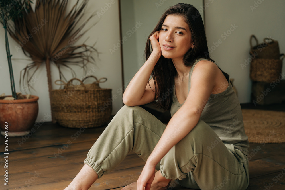 Fototapeta premium Portrait of a serene beautiful young brunette woman sitting on the floor.