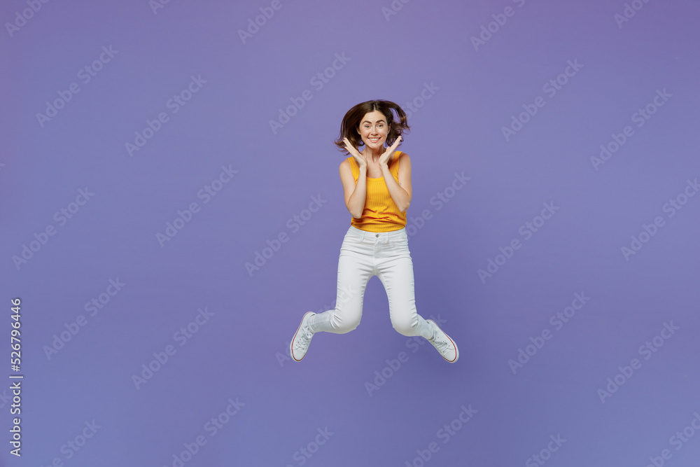 Full body young overjoyed surprised excited happy fun woman 20s she in yellow tank shirt jump high hold face isolated on plain pastel light purple background studio portrait People lifestyle concept