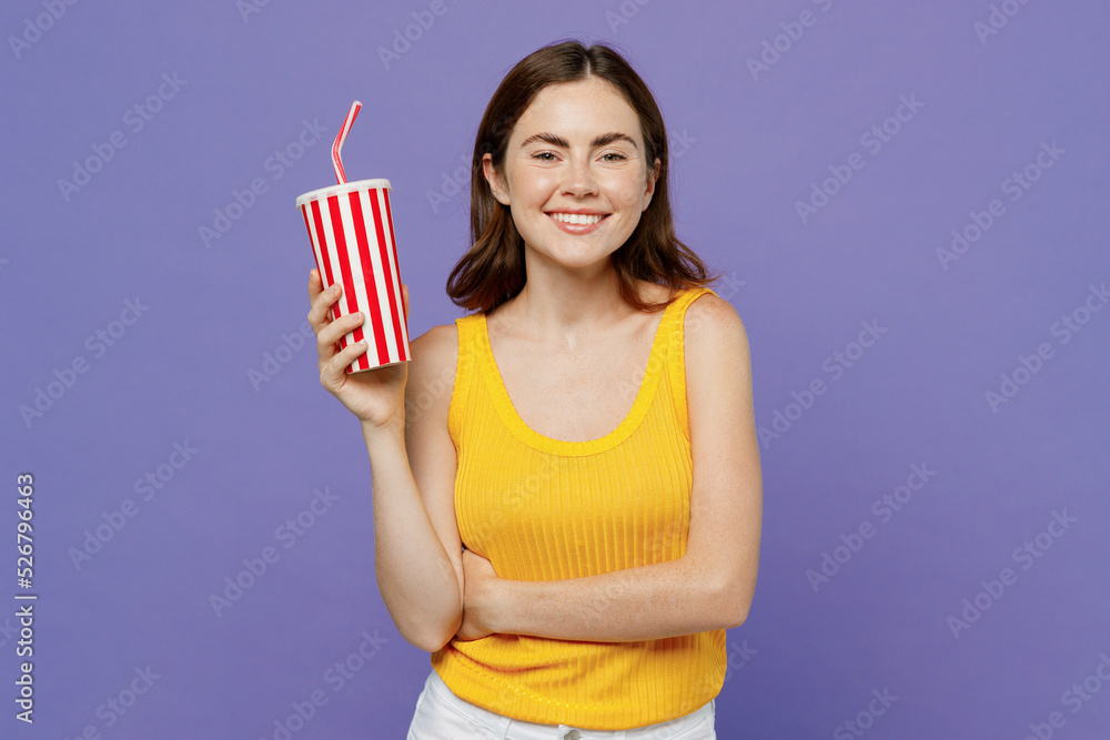 Young smiling happy cheerful fun cool woman 20s she in yellow tank shirt hold cup of soda pop fizzy water look camera isolated on plain pastel light purple background studio People lifestyle concept Young smiling happy cheerful fun cool woman 20s she in yellow tank shirt hold cup of soda pop fizzy water look camera isolated on plain pastel light purple background studio People lifestyle concept