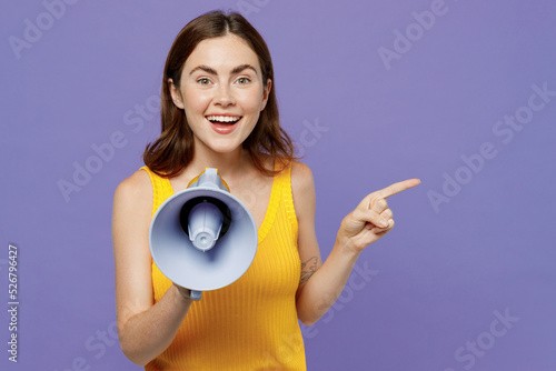 Young surprised woman 20s she wear yellow tank shirt hold scream in megaphone announces discounts sale Hurry up point finger aside on workspace isolated on plain pastel light purple background studio.
