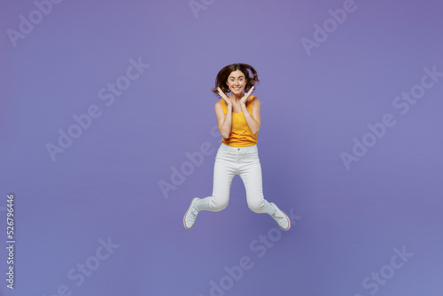 Full body young overjoyed surprised excited happy fun woman 20s she in yellow tank shirt jump high hold face isolated on plain pastel light purple background studio portrait People lifestyle concept