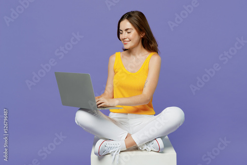 Full body young programmer freelancer woman 20s she in yellow tank shirt hold use work on laptop pc computer isolated on plain pastel light purple background studio portrait People lifestyle concept