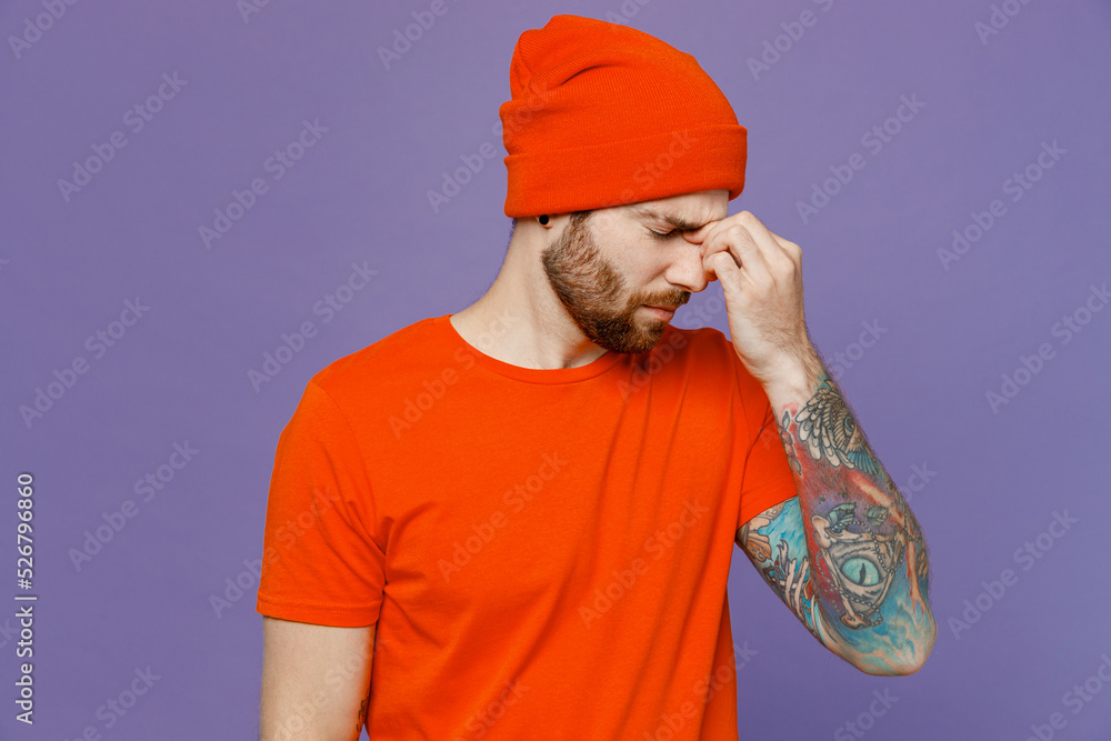 Young sad sick ill tired dissatisfied man 20s he wear red hat t-shirt keep eyes closed rub put hand on nose isolated on plain pastel light purple background studio portrait. People lifestyle concept. Young sad sick ill tired dissatisfied man 20s he wear red hat t-shirt keep eyes closed rub put hand on nose isolated on plain pastel light purple background studio portrait. People lifestyle concept.