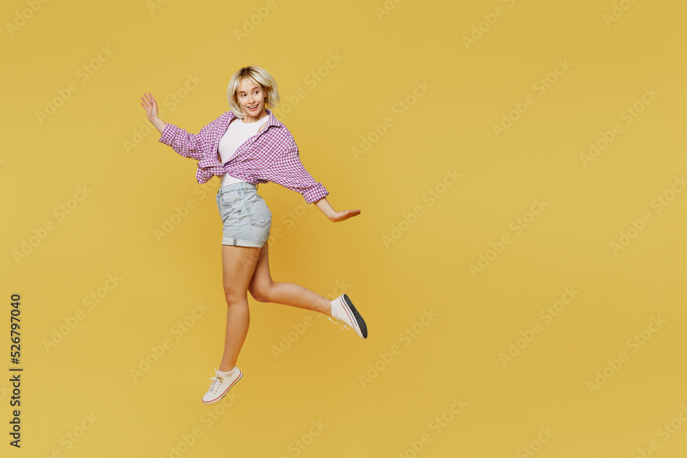 Full body side view young smiling happy fun blonde woman 20s she wear pink tied shirt white t-shirt walking go look aside jump high isolated on plain yellow background studio. eople lifestyle concept Full body side view young smiling happy fun blonde woman 20s she wear pink tied shirt white t-shirt walking go look aside jump high isolated on plain yellow background studio. eople lifestyle concept