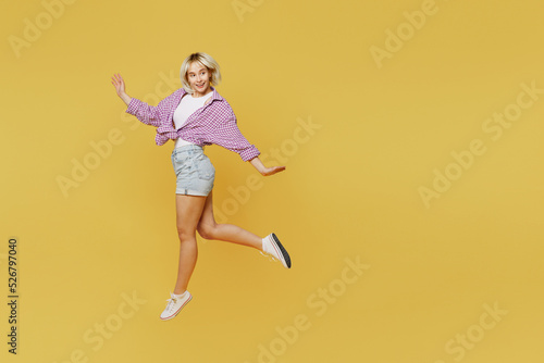 Full body side view young smiling happy fun blonde woman 20s she wear pink tied shirt white t-shirt walking go look aside jump high isolated on plain yellow background studio. eople lifestyle concept