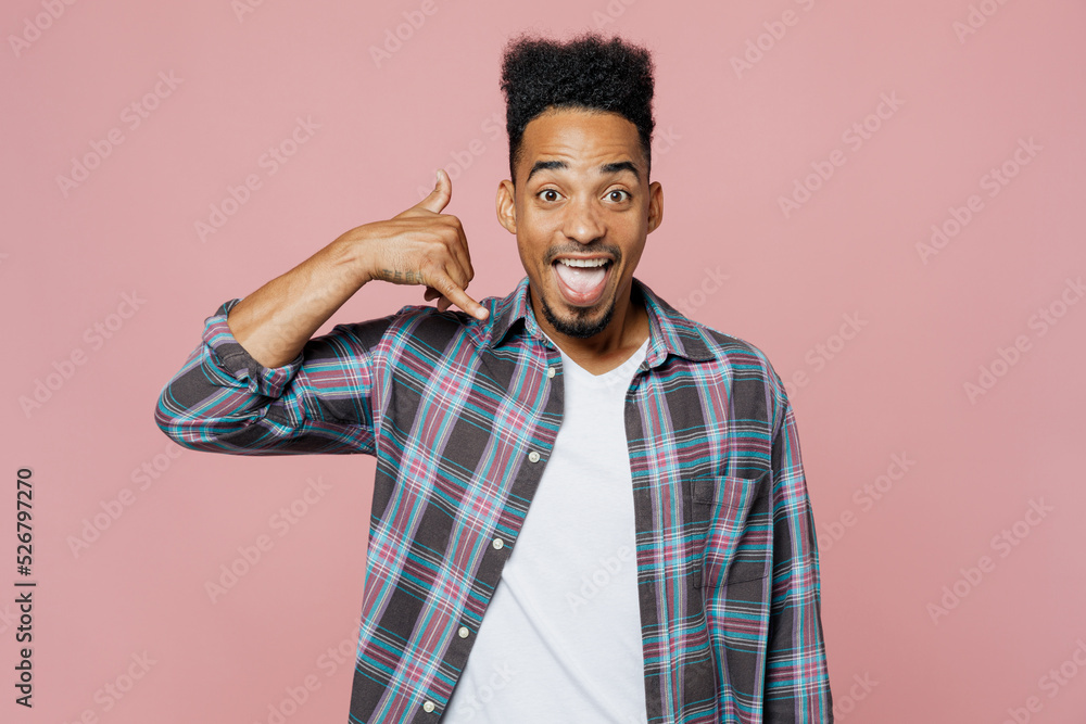 Young smiling happy man of African American ethnicity 20s he wear blue shirt doing phone gesture like says call me back isolated on plain pastel light pink background studio. People lifestyle concept. Young smiling happy man of African American ethnicity 20s he wear blue shirt doing phone gesture like says call me back isolated on plain pastel light pink background studio. People lifestyle concept.