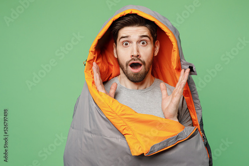 Young surprised traveler white man wrapped in sleeping bag look camera isolated on plain green background Tourist lead active healthy lifestyle walk on spare time Hiking trek rest travel trip concept
