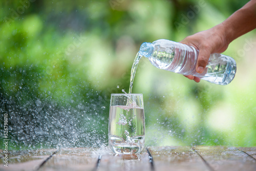 Clean drinking water is poured into a glass placed on a wooden stick with a spray of water spreading.