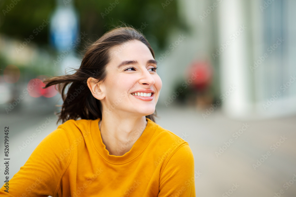 Happy young woman sitting outside and looking away
