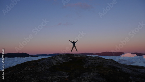 Person silhouette jumping in the air with icebergs in the back in Greenland