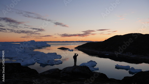 Person staring into the distance on hill with icebergs in Greenland