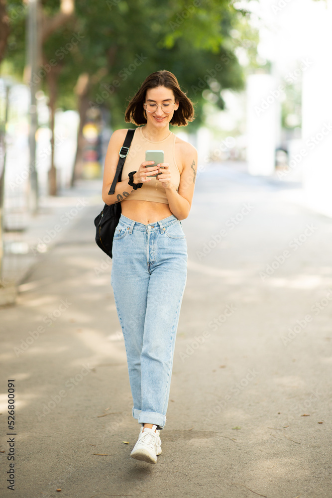 Attractive  young woman walking with bag and cellphone outdoors
