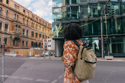 Photography back view of curly young woman with backpack standing on urban street in berlin