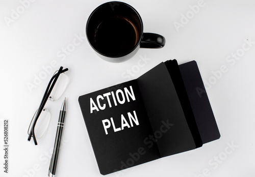 ACTION PLAN written text in small black notebook with coffee , pen and glasess on white background. Black-white style