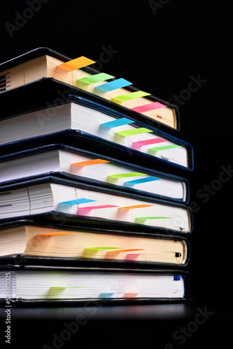 Close-up of a stack of office notepads with colorful sticky page markers sandwiched between pages on dark background
