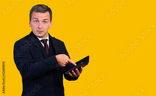 A young man holds a tablet computer in his hands and points his finger at it. . Isolated on yellow background.