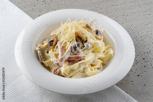Spaghetti with ham and champignon mushrooms sprinkled with cheese. On a white plate, black background. copyspace. photo