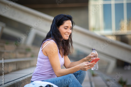Smiling woman using mobile phone while drinking water in city