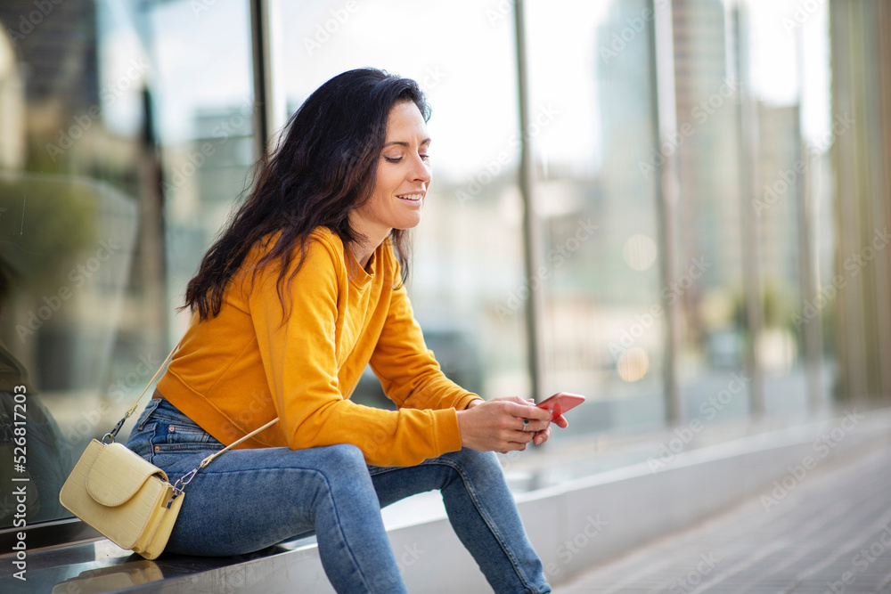 Smiling woman using smart phone sitting outdoors in city Smiling woman using smart phone sitting outdoors in city