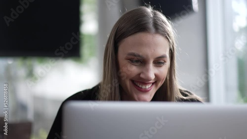 Happy young woman in front of computer seated at coffee shop. Girl liking content online browing insternet at cafe place. Person enjoying message notification photo