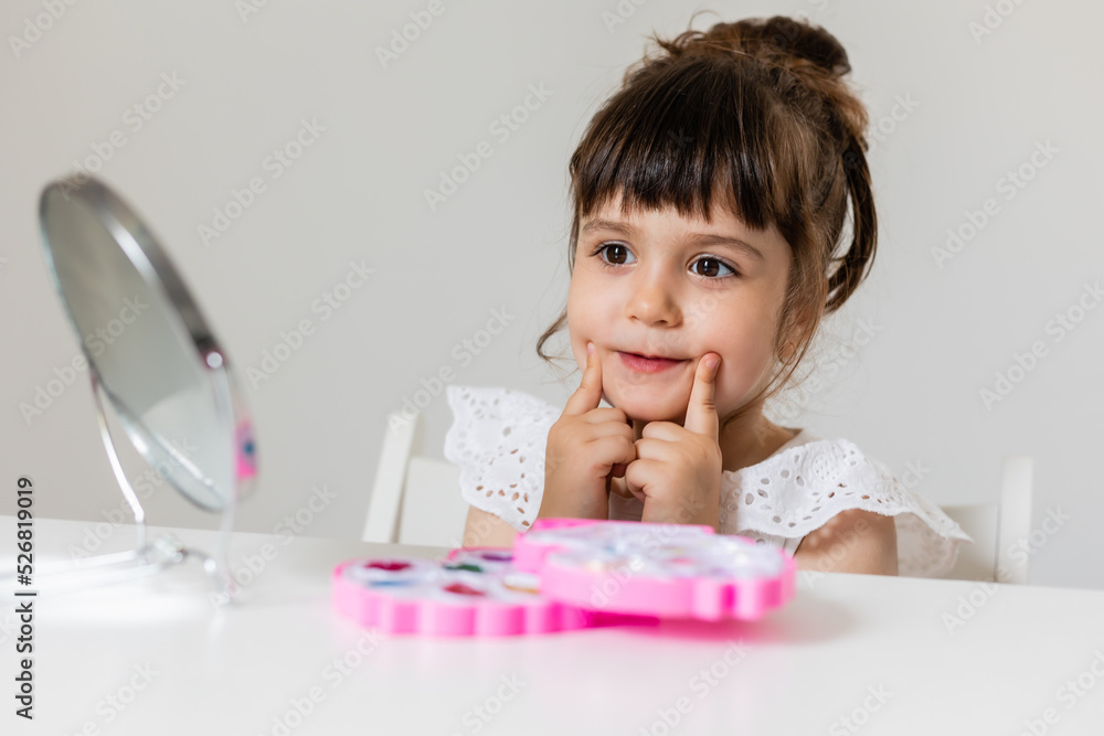 little girl is sitting at the dressing table in front of the mirror and applying makeup. like Mom little girl is sitting at the dressing table in front of the mirror and applying makeup. like Mom