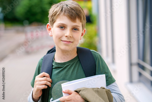 Happy preteen kid boy with backpack or satchel. Schoolkid in on the way to elementary or middle school on warm sunny summer day. Healthy child outdoors on the street in the city . photo