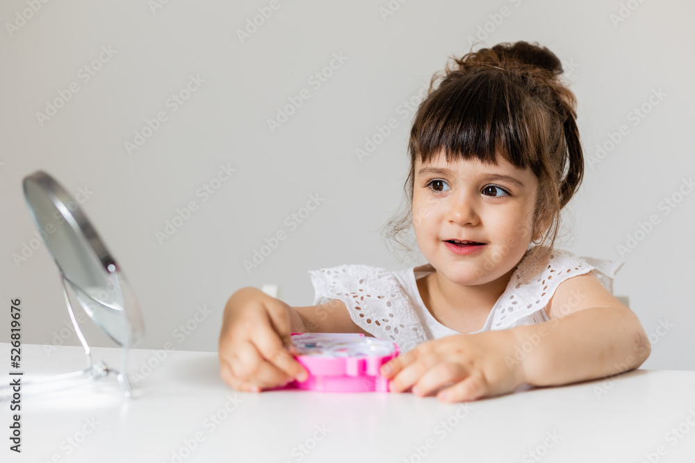 little girl is sitting at the dressing table in front of the mirror and applying makeup. like Mom little girl is sitting at the dressing table in front of the mirror and applying makeup. like Mom