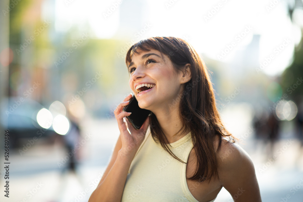 Cheerful young woman talking on phone while standing outdoors in the city Cheerful young woman talking on phone while standing outdoors in the city