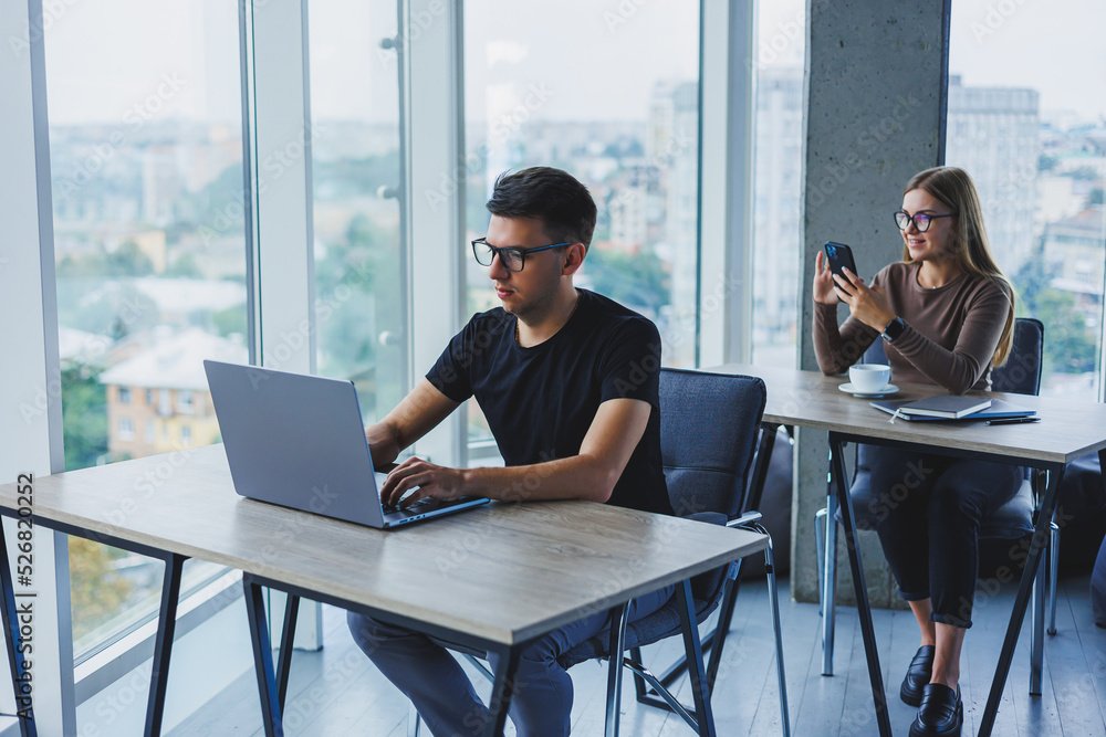 Young colleagues in the office at the desktop with a laptop. Young modern colleagues in smart casual clothes work while working in the office Young colleagues in the office at the desktop with a laptop. Young modern colleagues in smart casual clothes work while working in the office