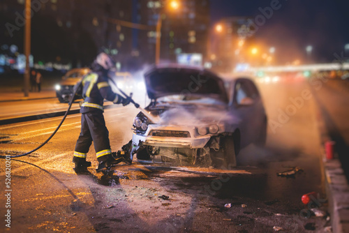 Group of fire men extinguishing and put out burning car crash after road traffic Fototapet