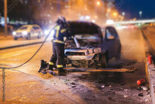 Group of fire men extinguishing and put out burning car crash after road traffic incident  fire fighting operation in the night city  firefighters with fire engine truck vehicle  emergency and rescue