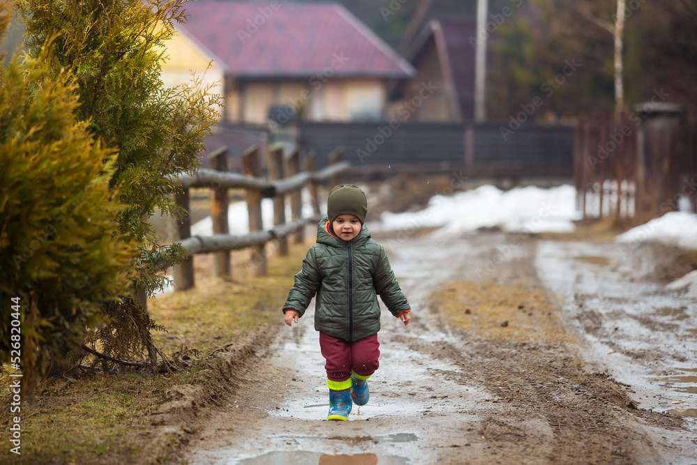 Little boy in protective rubber boots and rain clothes jumping in mud puddle. Happy child having fun while playing in puddle after rain. Little boy in protective rubber boots and rain clothes jumping in mud puddle. Happy child having fun while playing in puddle after rain.