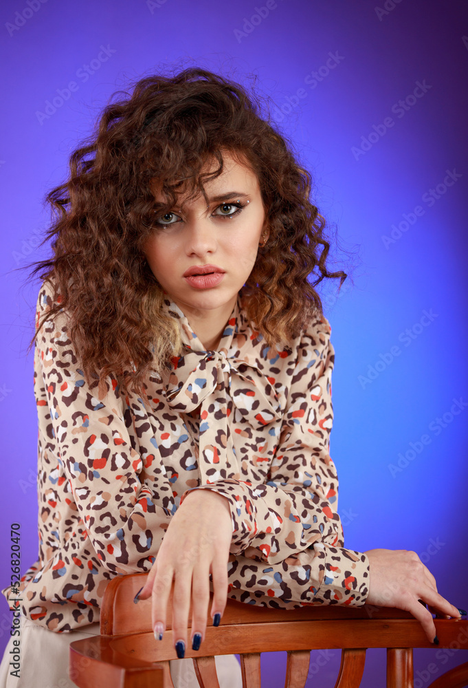 Close-up photo of young lady sittig on a chair and looking at the camera. Young beautiful curly-haired girl. Close-up photo of young lady sittig on a chair and looking at the camera. Young beautiful curly-haired girl.