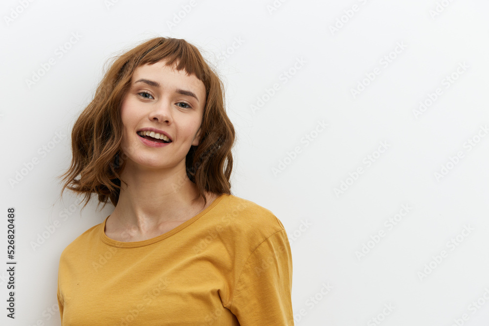 a beautiful, joyful woman is standing on a light background in a yellow T-shirt and smiling happily at the camera a beautiful, joyful woman is standing on a light background in a yellow T-shirt and smiling happily at the camera