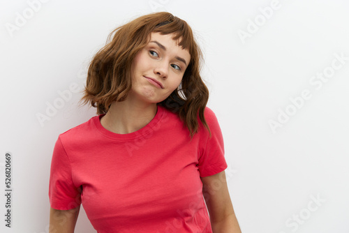 a funny, sweet, emotional woman in a red T-shirt stands on a white background and looks thoughtfully towards an empty space. Horizontal studio photo with a place to insert an advertising layout