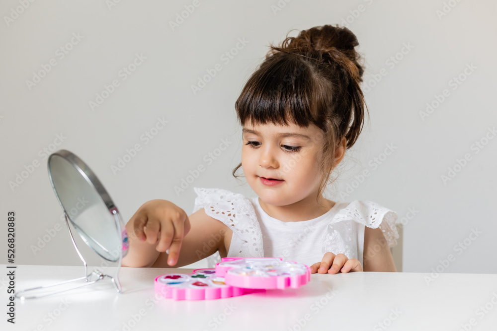 little girl is sitting at the dressing table in front of the mirror and applying makeup. like Mom little girl is sitting at the dressing table in front of the mirror and applying makeup. like Mom