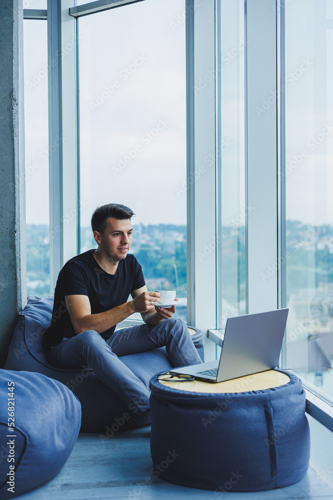 Smiling businessman looking for something and typing on a laptop and drinking fresh black coffee. The concept of a modern successful person. Young focused guy with glasses in an open office