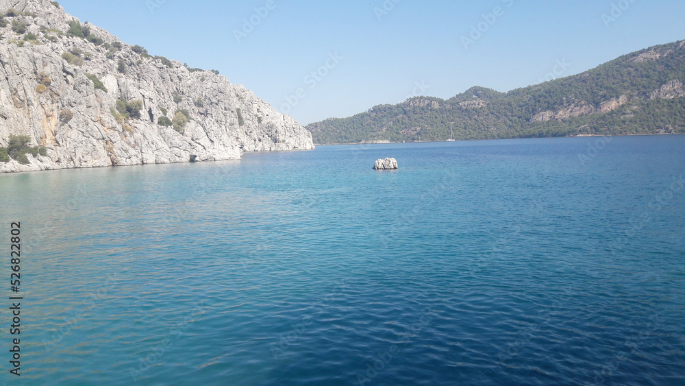 Transparent blue water of the Aegean Sea against the background of a rock. Beautiful tourist landscape of Turkey. Leisure, travel, tourism.