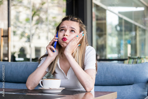 Tired young lady talking on the phone and sitting at the restaurant photo