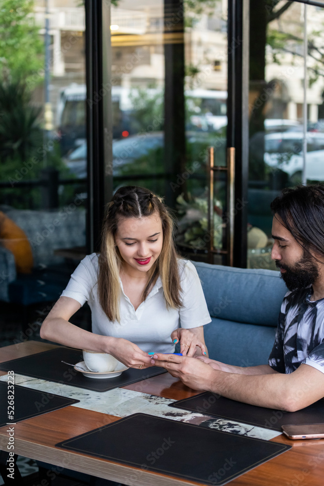 Fototapeta premium Young couple sitting at the restaurant and looking at phone