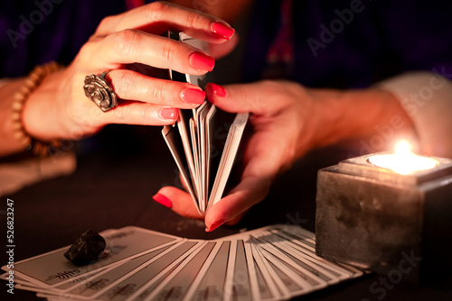 Fortune teller female hands shuffling a deck of tarot cards, during a reading. Close-up with candle light, moody atmosphere. photo