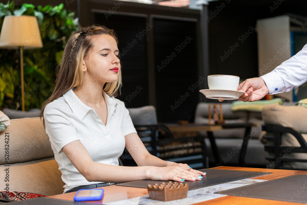 Fototapeta premium A waiter giving a cup of coffee to the young girl at the restaurant