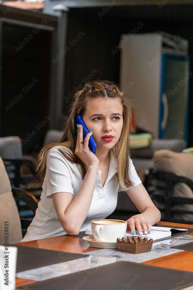Vertical photo of young lady sitting at the restaurant and talking on the phone Vertical photo of young lady sitting at the restaurant and talking on the phone