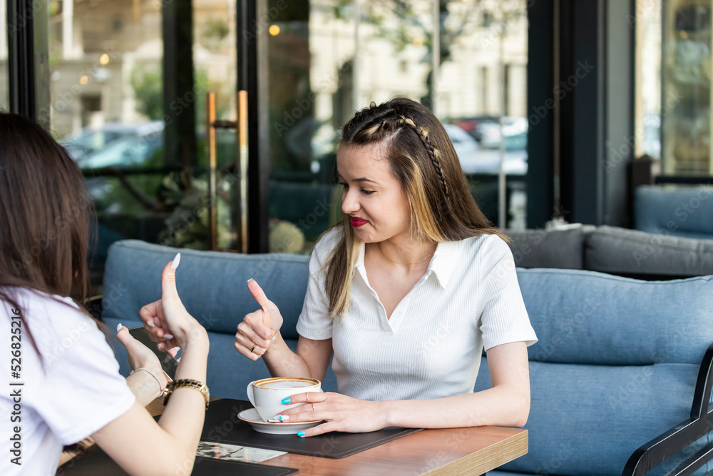 Young ladies sitting at the restaurant and gesture thumbs up Young ladies sitting at the restaurant and gesture thumbs up