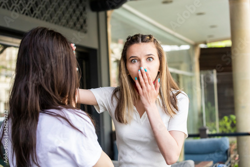 Young shocked blonde stand with fer friend and put her hand to her mouth