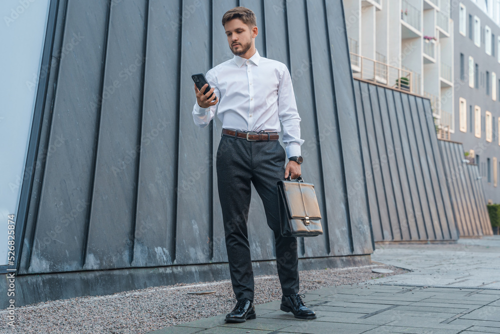 Portrait of male businessperson dressed in formal clothes using phone outdoors in city. Portrait of male businessperson dressed in formal clothes using phone outdoors in city.